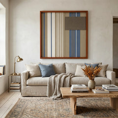 Large square Coastal Diary hand-woven wall art hanging elegantly above a cozy beige sofa decorated with blue throw pillows in a bright, modern living room.