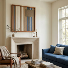 Beautiful framed hand-woven textile wall art styled elegantly above a modern minimalist fireplace mantel in a bright living room featuring a classic blue sofa.