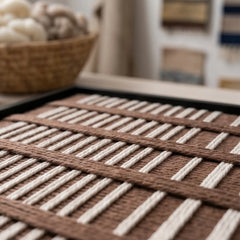Angled close-up shot of the Cocoa Cadence textile art lying flat on a table, showcasing the raised dimensional brown and cream hand-woven wool texture.