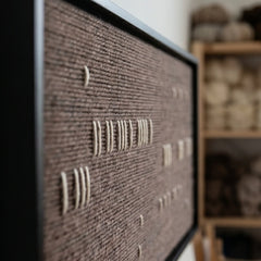 Extreme angled macro close-up of the Cocoa Whispers hand-woven wool tapestry highlighting small white stitches on a dark brown textured background.