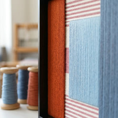 Close-up of Cold Fire fiber art in a studio setting, highlighting the intricate hand-wrapped red and blue yarn textures in a black frame.