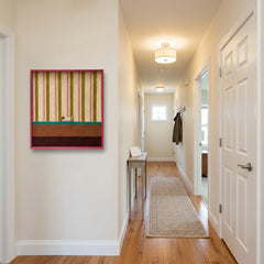 Framed striped and color-blocked textile art displayed on the left wall of a bright minimalist hallway.