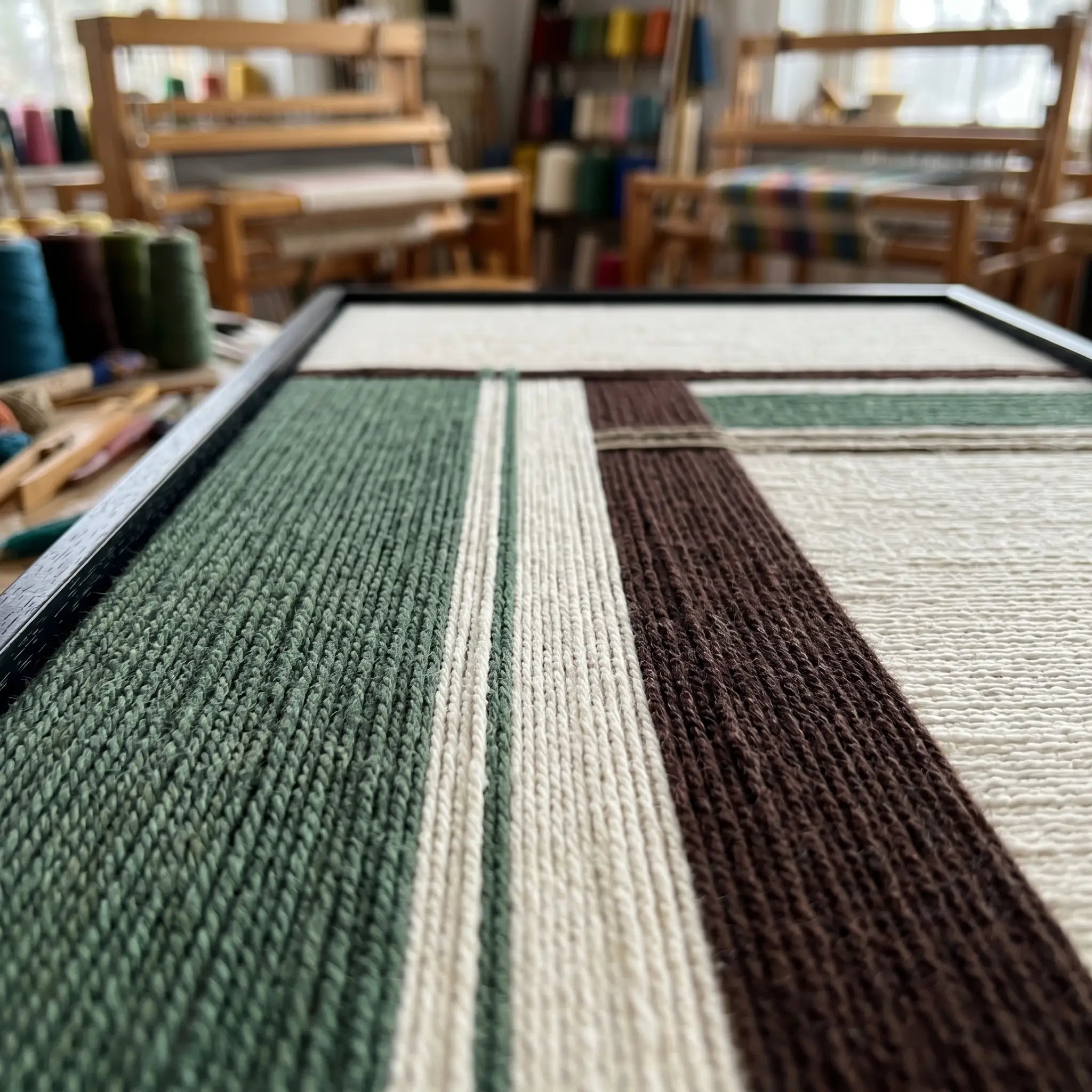 Low-angle perspective view of the hand-woven wool tapestry in an artist studio, showcasing the rich texture and precise yarn layering.