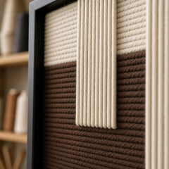 Angled close-up of the black frame and dimensional cream and dark brown hand-woven wool tapestry texture.