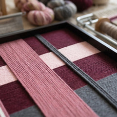 Detailed macro shot of the Lilac Whispers fiber art highlighting the intricate hand-wrapped plum and pink wool yarn textures in a black frame.