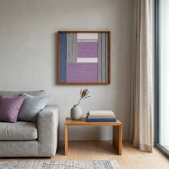 Framed textured fiber wall art hanging in a bright contemporary living room above a wooden side table and grey sofa.
