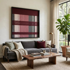 Striking square hand-woven wool tapestry positioned perfectly above a classic grey sofa and a wooden coffee table in a sunlit modern living room.