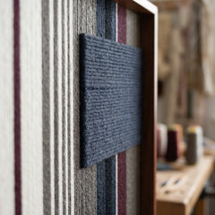 Angled close-up of the framed Midnight Fjord hand-woven tapestry showcasing the wooden frame and dimensional dark navy patch against striped wool.