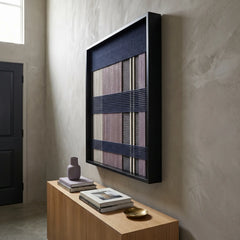 Angled view of the framed Midnight Lavender textile wall art hanging gracefully on a textured wall above a minimalist light wood console table.
