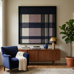 Framed Midnight Lavender textile wall art displayed in a bright living room, hanging above a wooden media console next to a cozy navy blue armchair with a white throw.