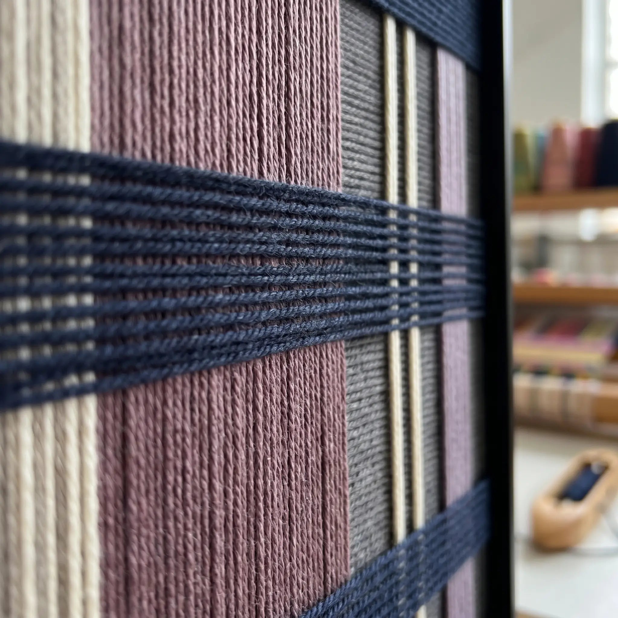 Extreme angled macro close-up of the Midnight Lavender hand-woven textile art highlighting the textured navy blue horizontal yarn crossing over lavender and cream vertical stripes.