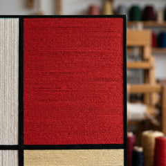Macro close-up of the vibrant red wool fibers and thick black lines of the hand-woven geometric wall art tapestry.
