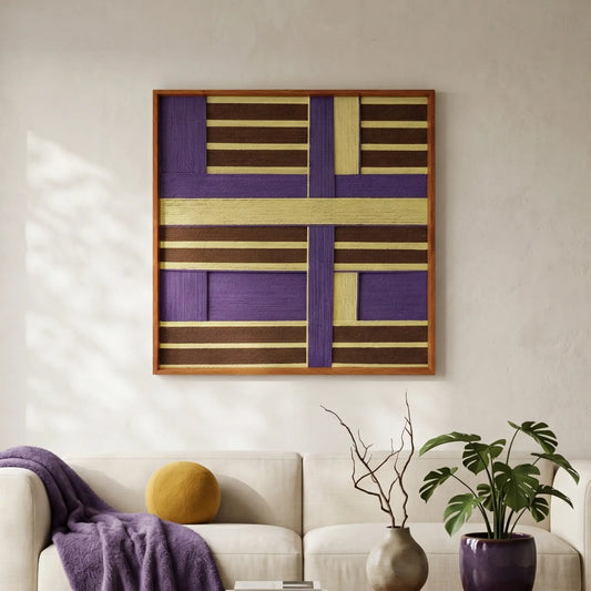 Square hand-woven wool wall art with a bold purple and gold geometric block pattern in a wood frame, styled above a white sofa with a purple throw blanket.