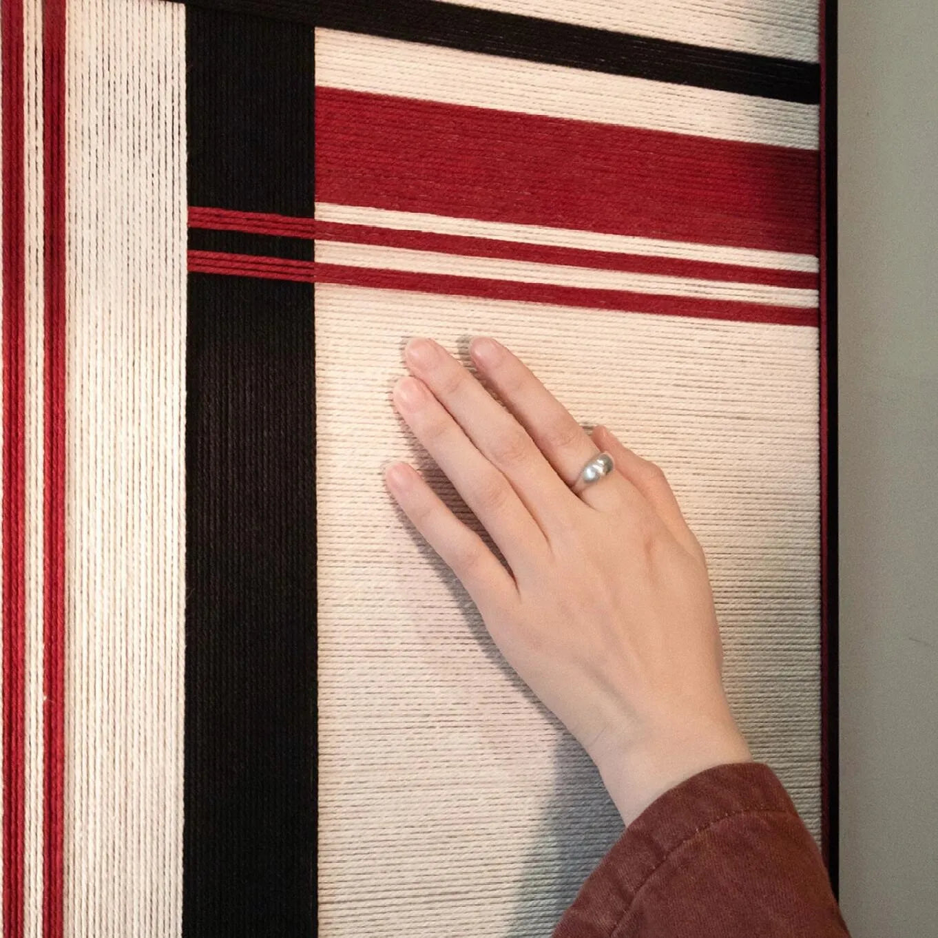 Close-up of “Napoli” yarn wall art capturing the tactile looped wool and the contrast between red and black stripe fibers
