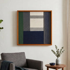 Modern hand-woven wool tapestry in navy and forest green tones hanging on a white wall in a minimalist living room setting.