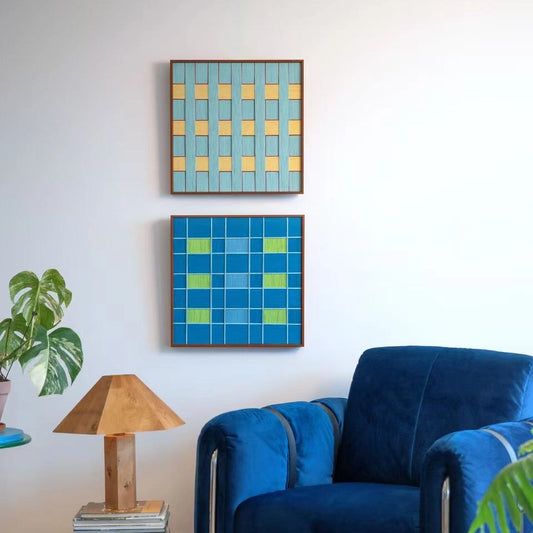 Two framed "North Sea Poem" hand-woven wall art pieces hanging vertically above a blue velvet sofa, featuring checkerboard patterns in blue and yellow tones.