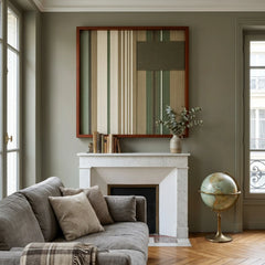 Striking square hand-woven wool tapestry positioned perfectly above a classic white fireplace mantel in a moody room with olive green walls and a grey sofa.