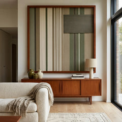 The Olive Solitude green and beige hand-woven wool tapestry provides a serene focal point over a wooden console behind a comfortable white sofa.