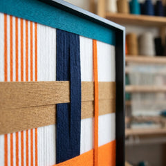 Side profile view of the framed wool tapestry showing the sleek black metal frame and the dimensional depth of the woven textile layers.