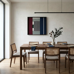 Large square hand-woven wool wall art with navy, burgundy, and grey geometric patterns hanging in a modern dining room with a walnut table and cane chairs.