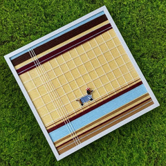 Hand-woven wool art placed on lush green grass, highlighting the organic texture and earthy tones of the framed tapestry.