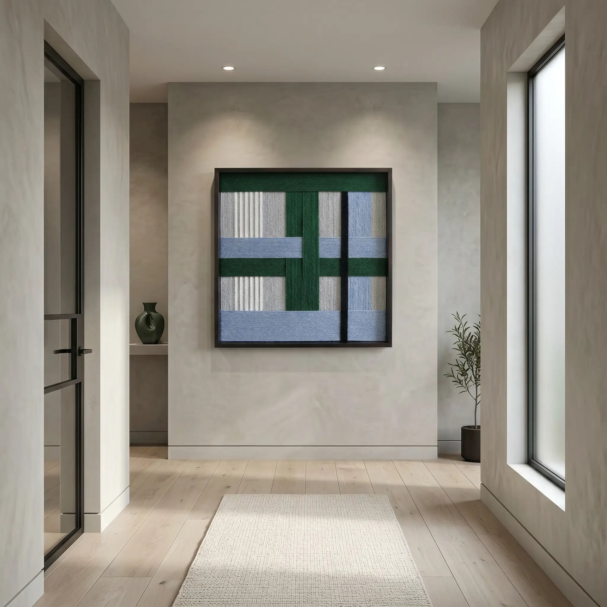 Modern framed wool tapestry hanging in an architectural space, showcasing the geometric contrast of forest green and sky blue tones.