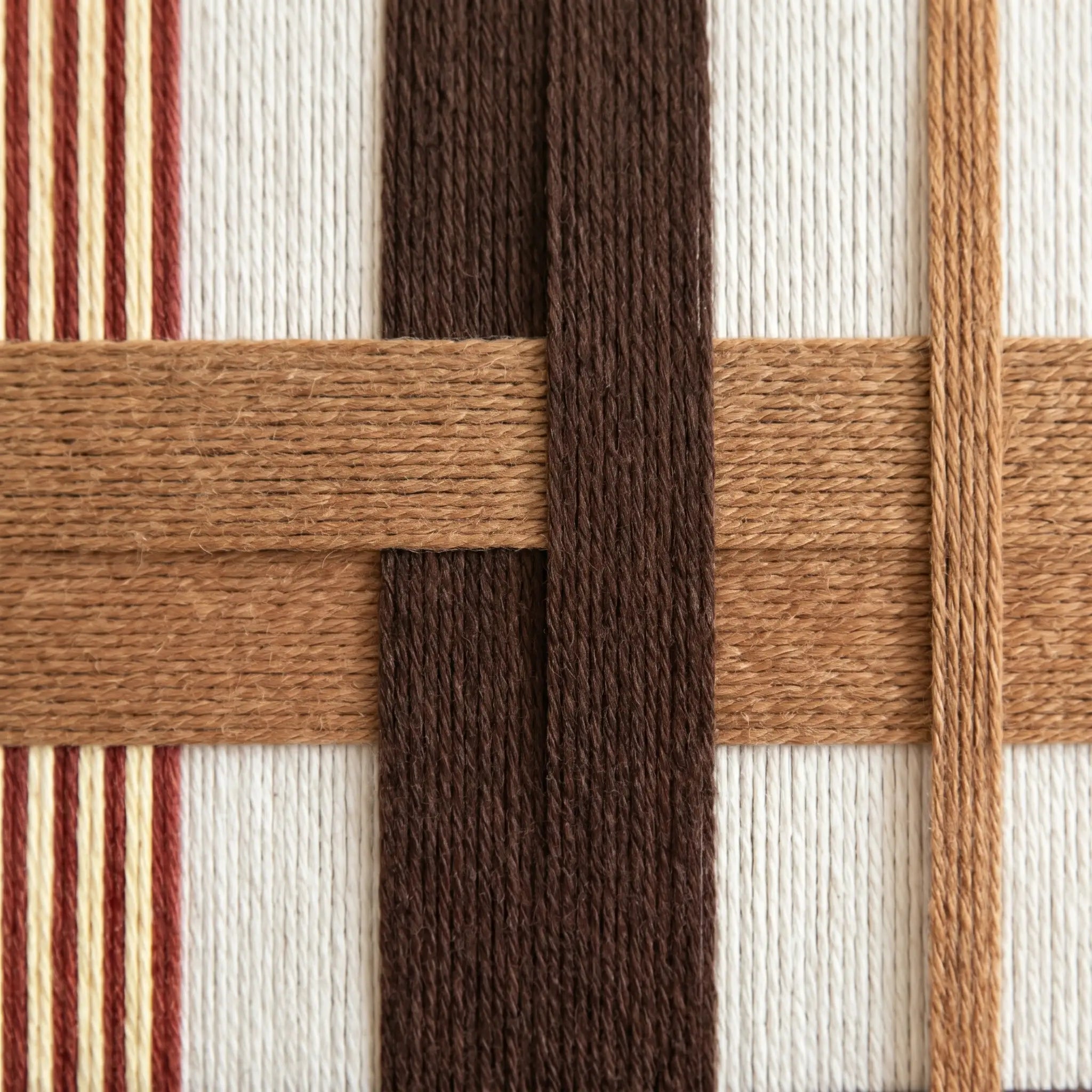 Macro shot of the hand-woven wool texture showing the intricate interlocking brown and terracotta yarn patterns.