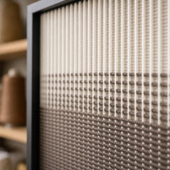 Angled close-up of the black frame and dimensional cream to brown gradient in this hand-woven wool tapestry.