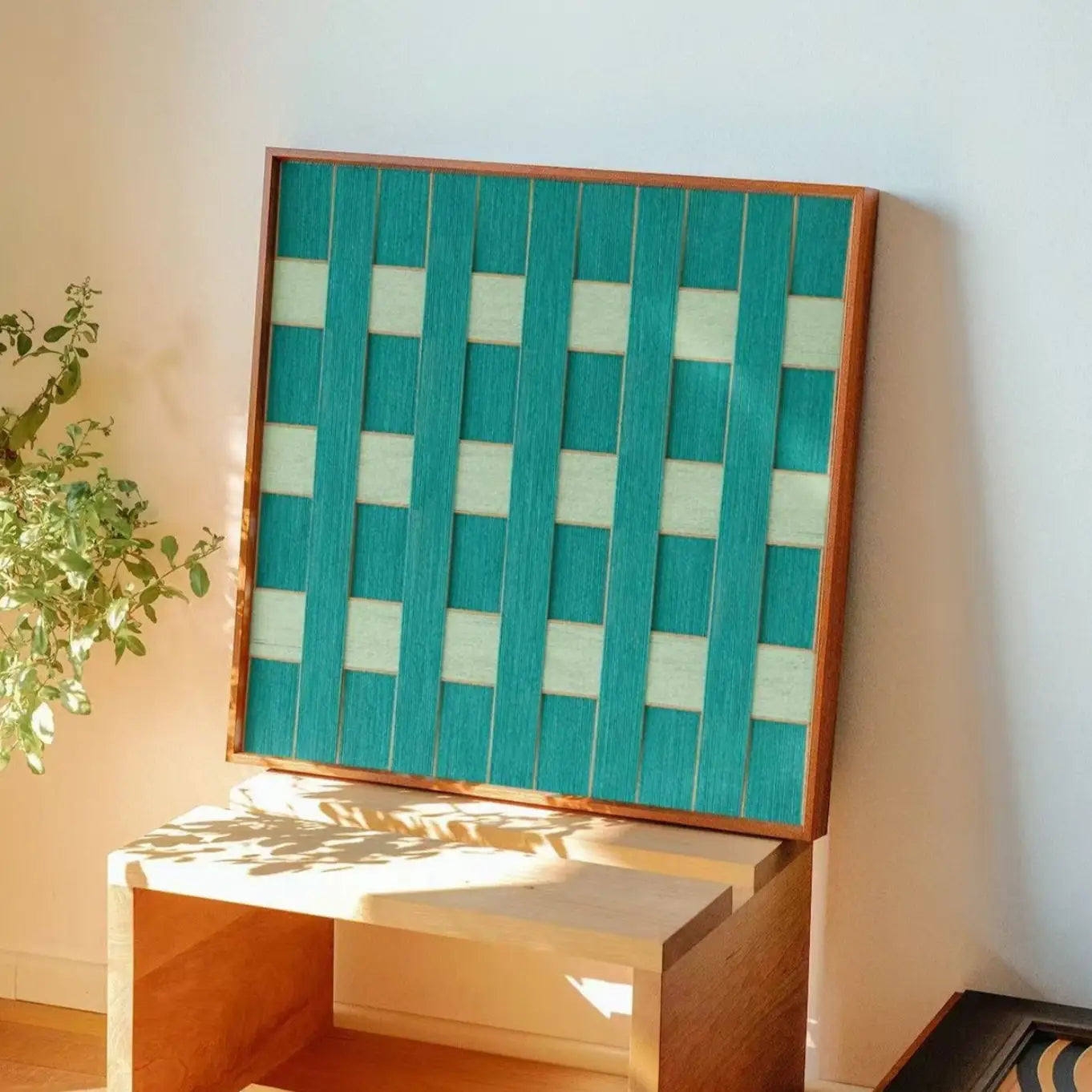 Handmade wool wall art piece leaning against a wall in a cozy home nook, reflecting natural sunlight and warm interior aesthetics.