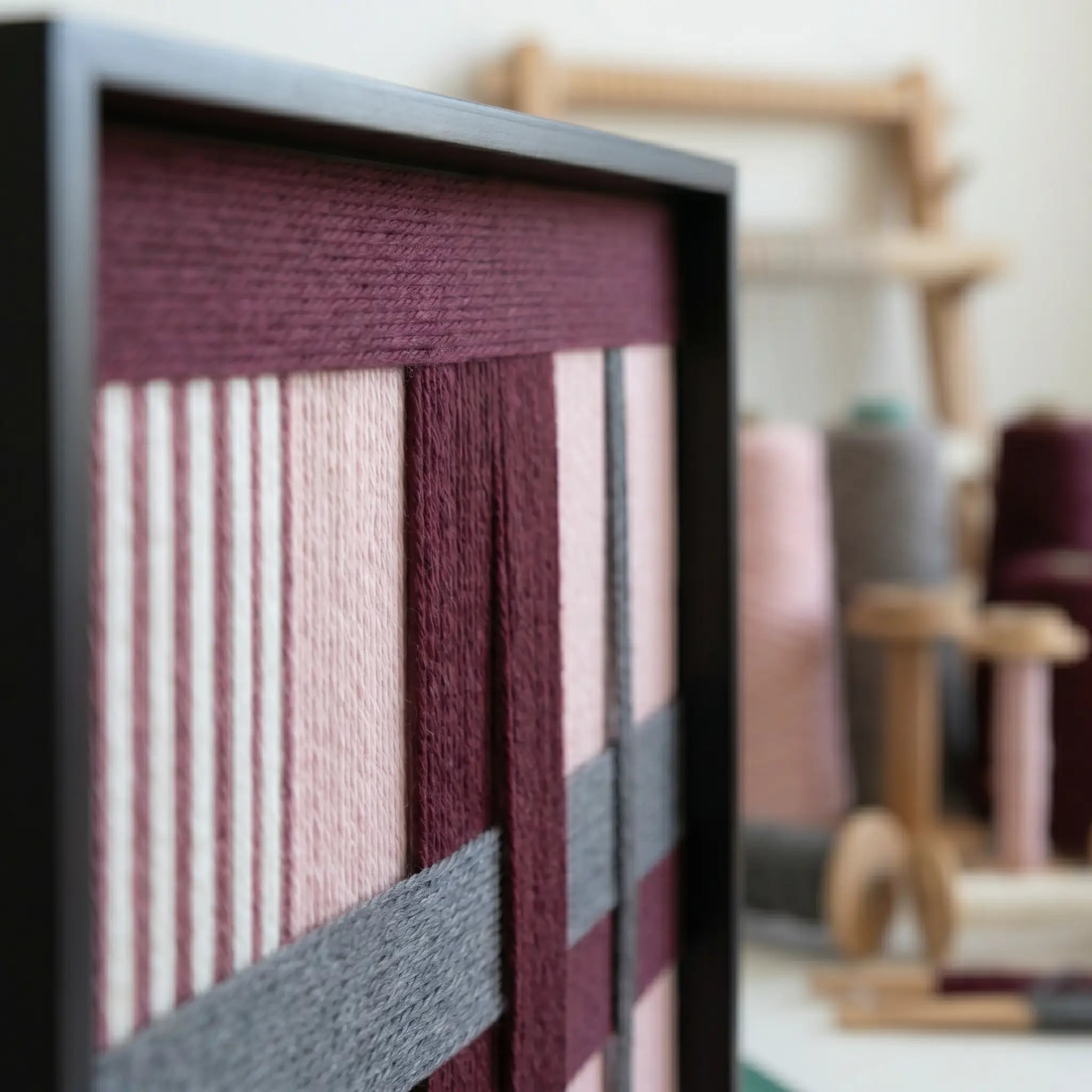 Close-up side view of Rose Coordinates hand-woven wool art showing the deep burgundy, dusty rose, and grey yarn textures in a sleek black frame.