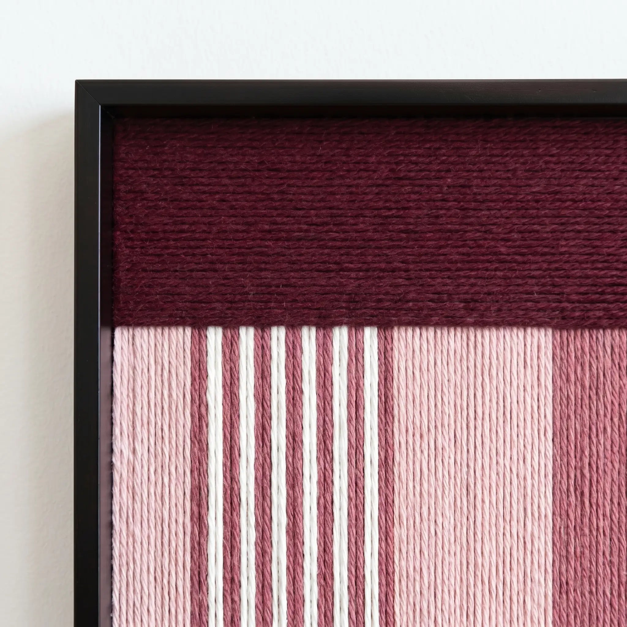Macro shot of the black metal frame corner highlighting the professional craftsmanship and rich burgundy wool fibers of the tapestry.