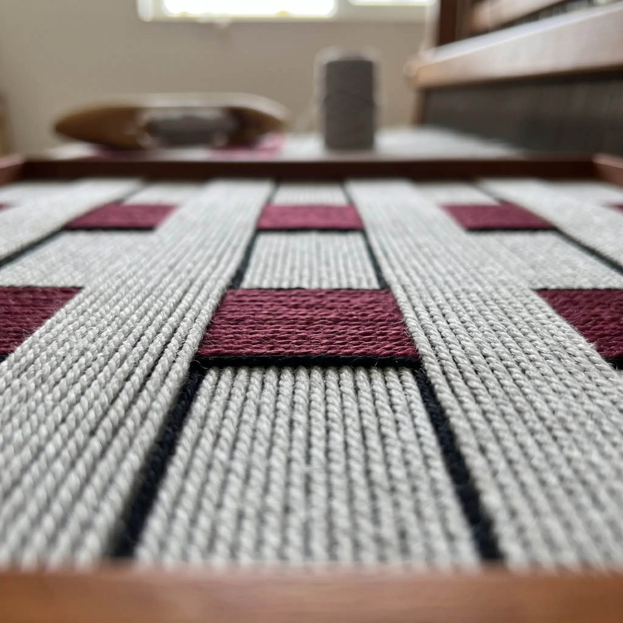 Extreme macro close-up of the Ruby Lattice fiber art, highlighting the intricate hand-wrapped grey and deep red wool yarn textures woven into a checkerboard pattern.