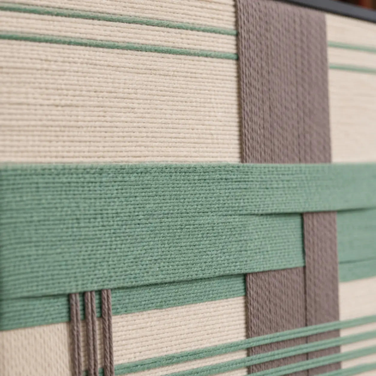 Detailed macro shot of the Sage Crossing hand-woven wool tapestry highlighting thick sage green and grey intersecting yarn textures.