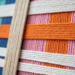 Framed colorful hand-woven wool wall art styled in a serene bedroom as a striking focal point above a warm wood bed frame.