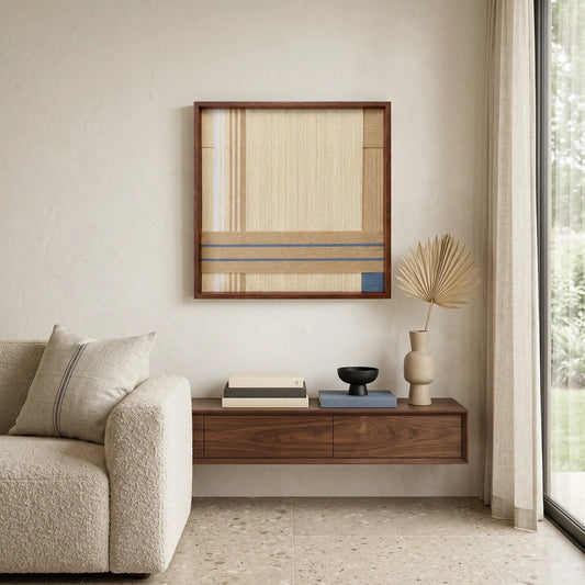 Large hand-woven wool wall art in beige and blue tones displayed above a floating walnut shelf in a minimalist living room.