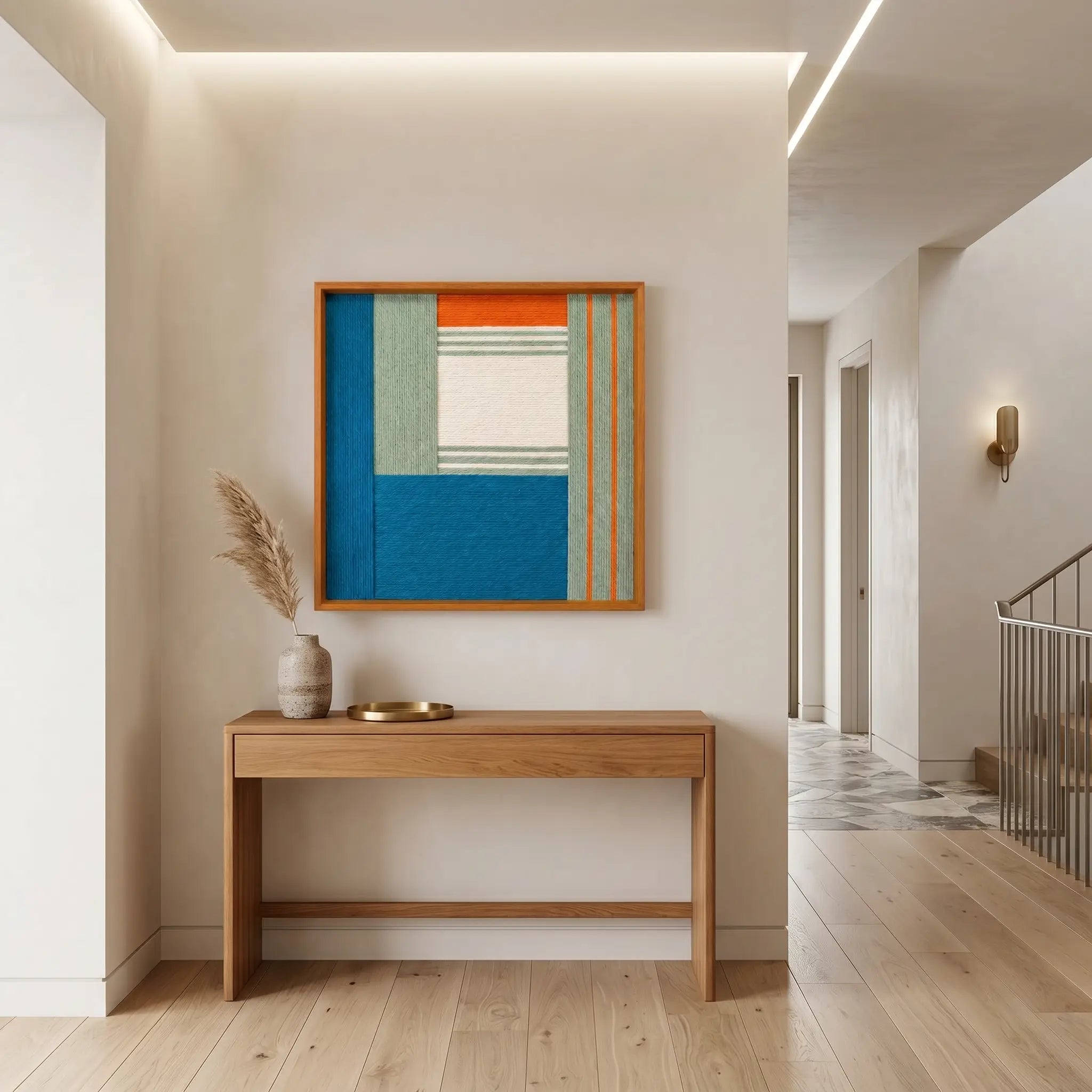 Framed textured fiber art creating a vibrant focal point in a minimalist home foyer above a simple light wood console table.