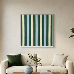 Square hand-woven wool wall art featuring vertical stripes in forest green, pale blue, and cream, hanging above a cream-colored sofa with green accent pillows.