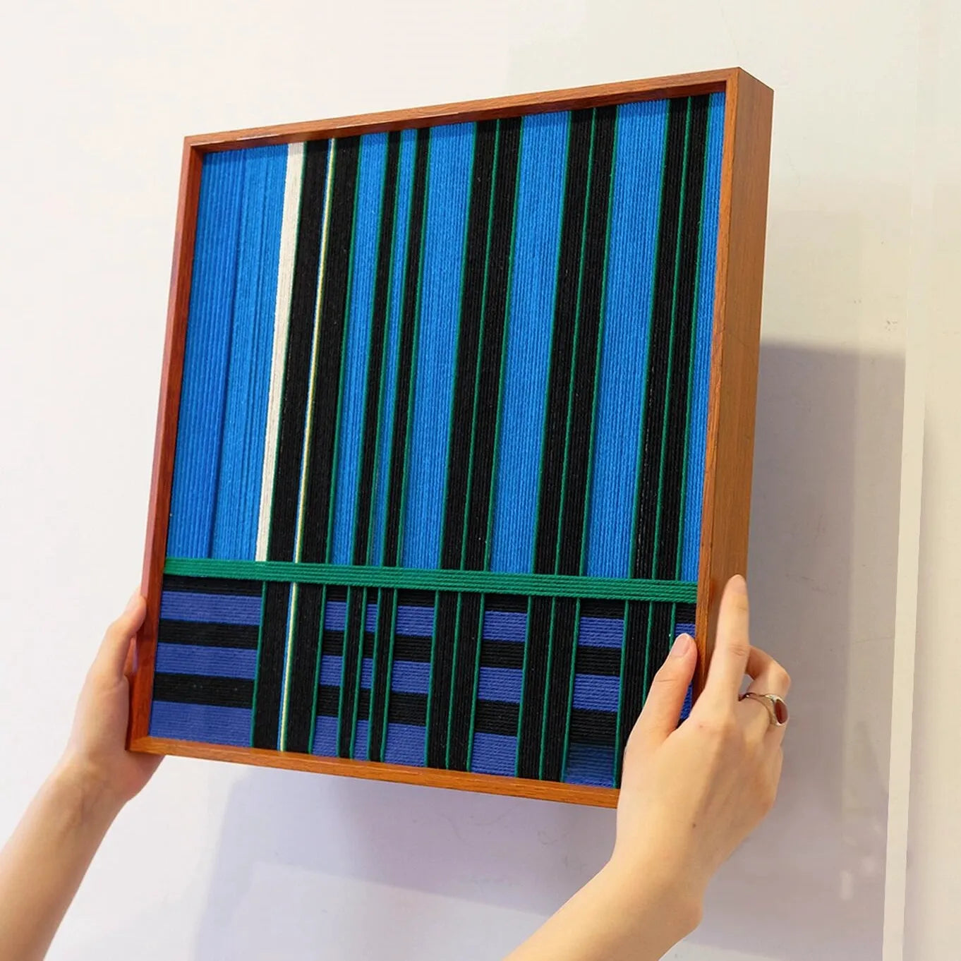 Hand-held view of Summer Night’s Serenity yarn woven wall art showing its exact square dimensions, crisp stripe pattern, and sturdy wooden frame
