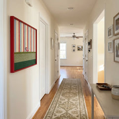 Angled perspective of the Tangerine Stripe Pup Venture textile wall art hanging on a white wall in a long, well-lit hallway corridor.