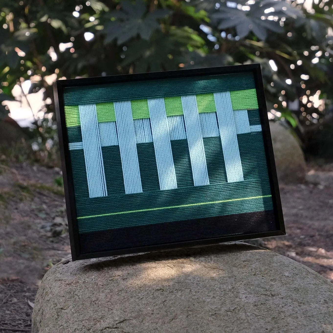 Velvet Vine yarn art displayed on a boulder, highlighting its sturdy black frame and alternating green-white stripe design
