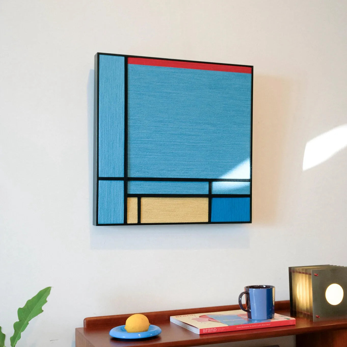 Vertical side view of Weave Reshape wall art showing the slim profile of its natural wood frame and the depth of colored yarn stripes.
