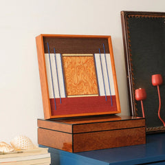 The Festive Harmony framed art leaning against a wooden box, demonstrating a casual and modern way to display fiber art on a desk or table.